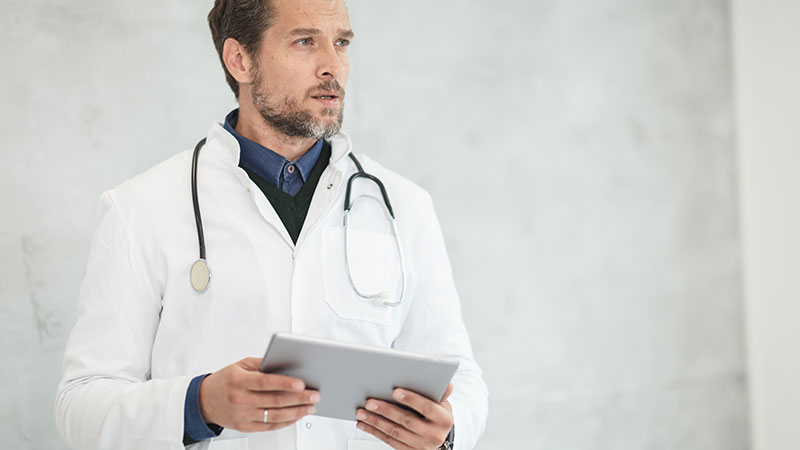 A doctor holding an iPad looking ahead.